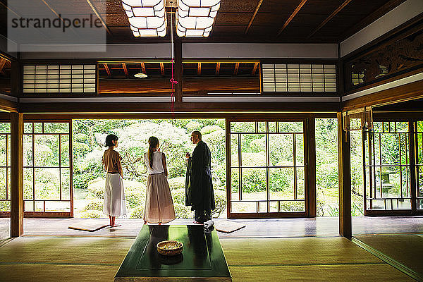 Buddhistischer Priester und zwei japanische Frauen stehen im buddhistischen Tempel.