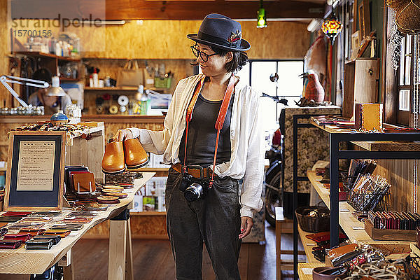 Japanische Frau mit Hut und Brille beim Stöbern in einem Ledergeschäft.