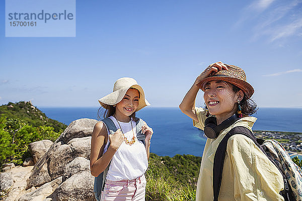 Zwei Japanerinnen mit Hüten stehen auf einer Klippe  im Hintergrund das Meer.