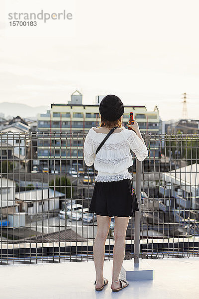 Rückansicht einer jungen Japanerin  die auf einem Dach in einer städtischen Umgebung steht.