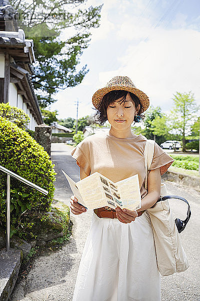 Japanische Frau mit Hut und Karte in der Hand vor einem buddhistischen Tempel stehend.