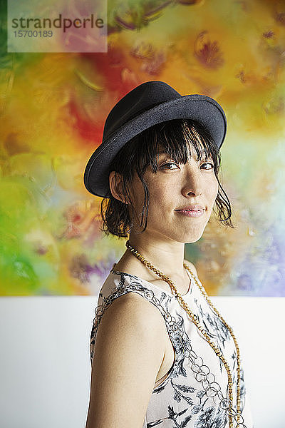 Japanische Frau mit Hut vor einem abstrakten Gemälde in einer Kunstgalerie.