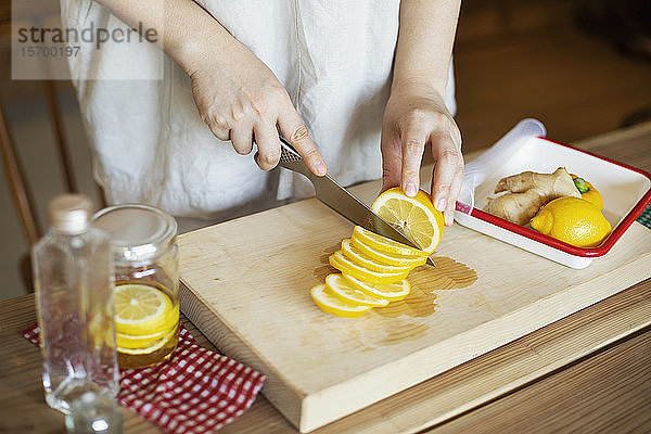 Hochwinkel-Nahaufnahme einer Person  die mit einem Messer auf einem hölzernen Schneidebrett Zitronen schneidet.