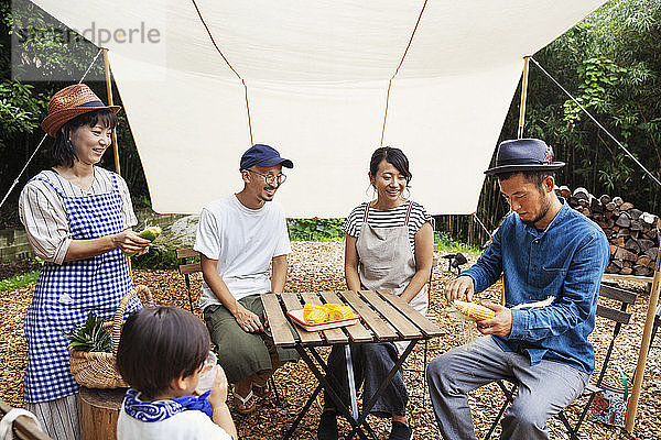 Eine Gruppe japanischer Männer und Frauen und ein Junge versammelten sich um einen Tisch unter einem Baldachin und bereiteten Gemüse zu.