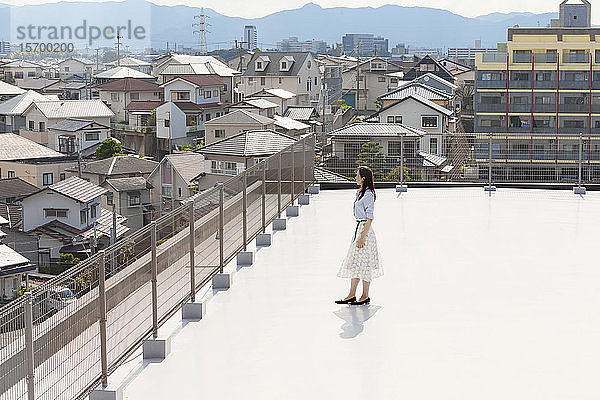 Hochwinkelaufnahme einer Japanerin  die auf einem Dach in einer städtischen Umgebung steht.