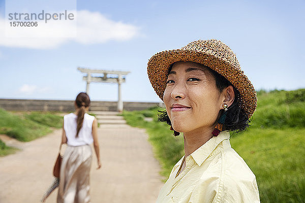 Zwei Japanerinnen mit Hüten stehen auf einem Weg  im Hintergrund der Shinto-Schrein.
