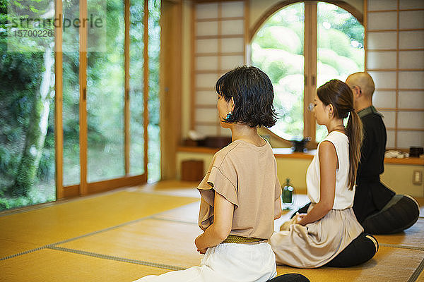 Zwei Japanerinnen und ein buddhistischer Priester knien im buddhistischen Tempel und beten.