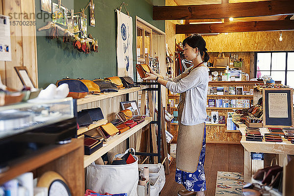 Japanerin mit Schürze  die in einem Ledergeschäft steht und eine Clutch Bag aus hellbraunem Leder hält.