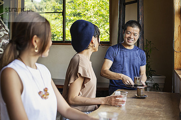 Kellner  der zwei Japanerinnen bedient  die an einem Tisch in einem japanischen Restaurant sitzen.