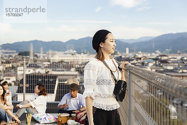 Lächelnde junge Japanerin  die auf einem Dach in einer städtischen Umgebung steht.