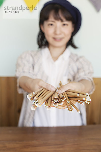 Japanerin  die in einem Hofladen hinter der Theke steht und einen Haufen Papprollen hält.