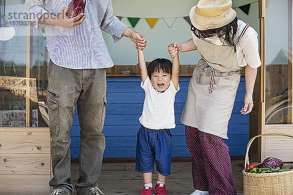Japanischer Mann  Frau und Junge stehen vor einem Bauernladen und halten Händchen.