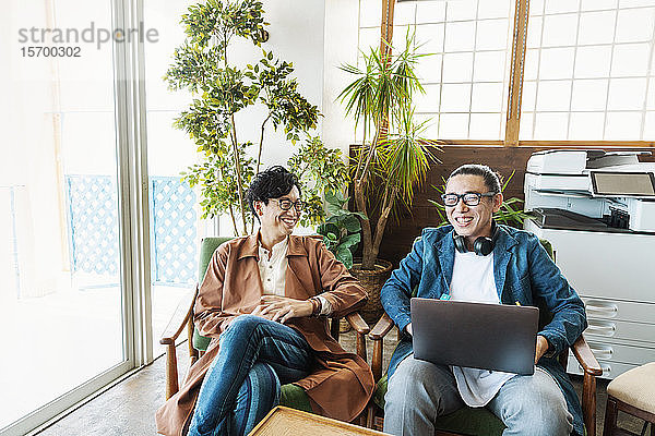 Zwei männliche japanische Berufstätige  die an Laptop-Computern in einem Raum für Zusammenarbeit arbeiten.