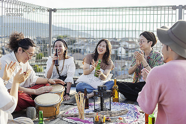 Gruppe junger japanischer Männer und Frauen  die auf einem Dach in einer städtischen Umgebung stehen.