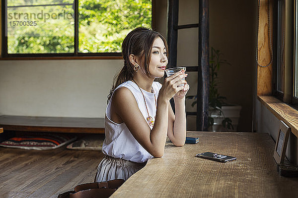 Lächelnde Japanerin  die an einem Tisch in einem japanischen Restaurant sitzt und trinkt.