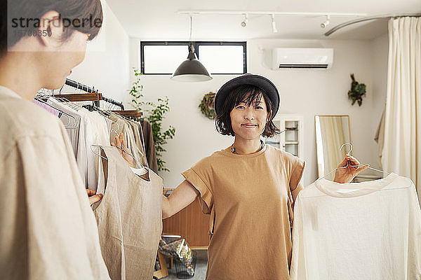 Zwei Japanerinnen stehen in einer kleinen Modeboutique und schauen auf Oberteile.