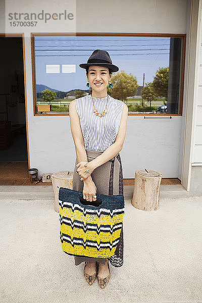 Porträt einer lächelnden Japanerin mit Hut und Einkaufstasche  die in die Kamera schaut.