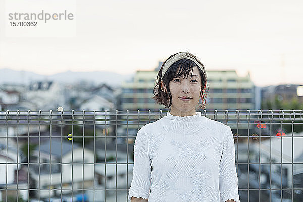 Japanerin  die auf einem Dach in einer städtischen Umgebung steht und in die Kamera schaut.