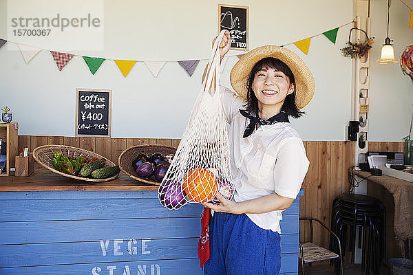 Japanische Frau mit Hut  die in einem Hofladen arbeitet und in die Kamera lächelt.