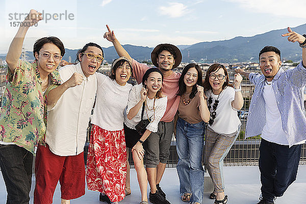 Lächelnde Gruppe junger japanischer Männer und Frauen  die auf einem Dach in einer städtischen Umgebung stehen.