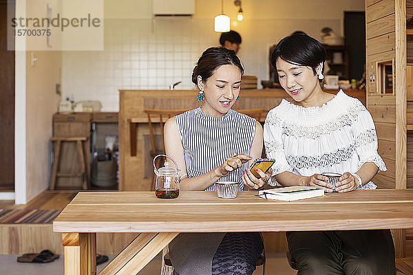 Zwei Japanerinnen sitzen an einem Tisch in einem vegetarischen Café und benutzen ein Mobiltelefon.
