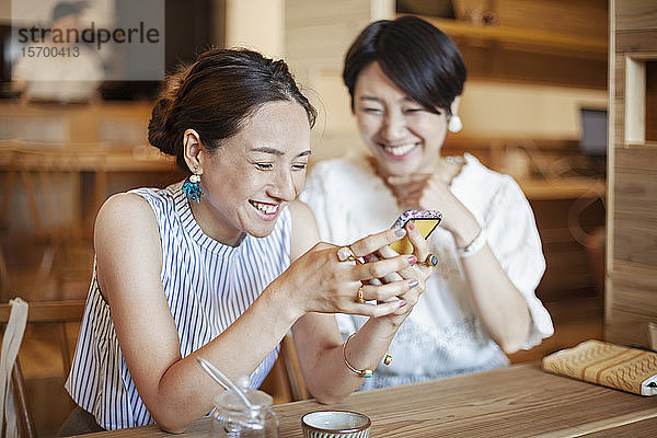 Zwei Japanerinnen sitzen an einem Tisch in einem vegetarischen Café und benutzen ein Mobiltelefon.