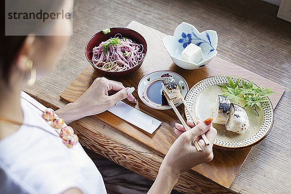 Schrägansicht einer Japanerin  die an einem Tisch in einem japanischen Restaurant sitzt und isst.