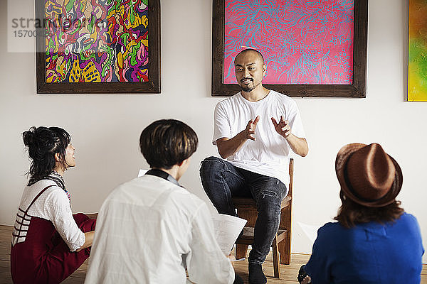 Gruppe japanischer Männer und Frauen  die in einer Kunstgalerie sitzen und eine Diskussion führen.