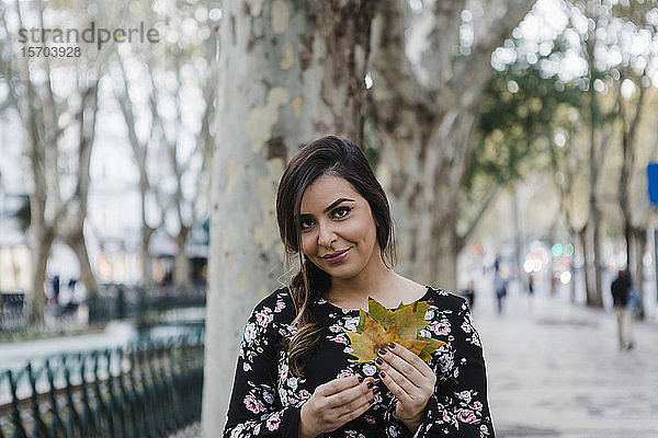 Porträt lächelnde junge Frau hält Herbstblätter im Stadtpark