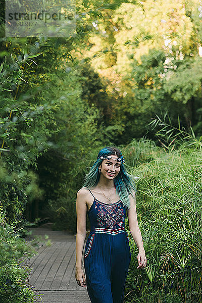 Porträt einer lächelnden  glücklichen jungen Frau mit blauem Haar  die einen Fußweg in einem üppigen Park entlanggeht