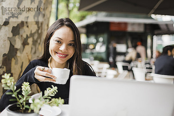 Porträt selbstbewusste Frau trinkt Kaffee am Laptop in einem Straßencafé