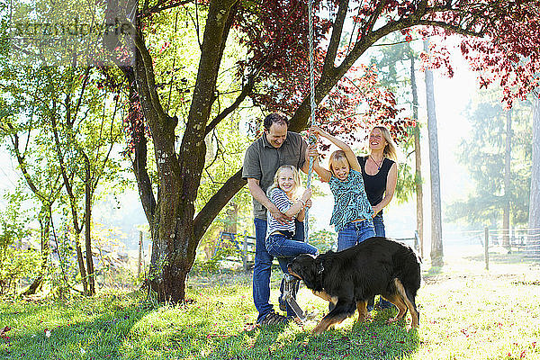 Glückliche Familie mit Hund spielt auf Seilschaukel in sonnigen Herbst Park