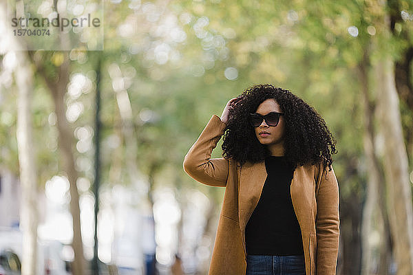 Stilvolle junge Frau mit Sonnenbrille geht im Park spazieren