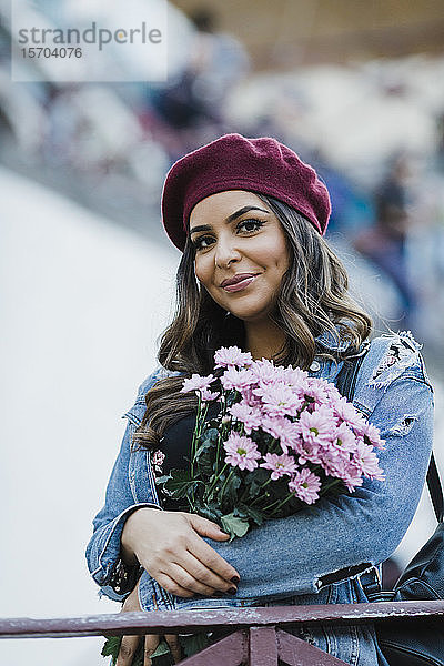Porträt einer lächelnden jungen Frau mit Baskenmütze  die einen Blumenstrauß hält