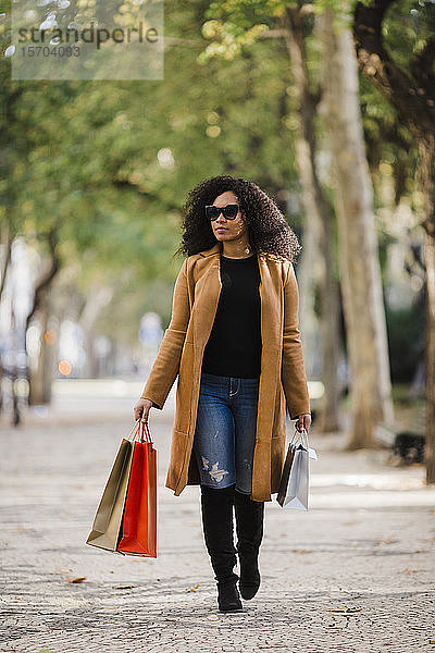 Stilvolle junge Frau mit Einkaufstaschen auf dem Gehweg