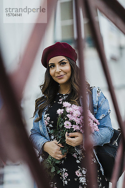 Porträt einer selbstbewussten jungen Frau mit Baskenmütze  die einen Blumenstrauß hält