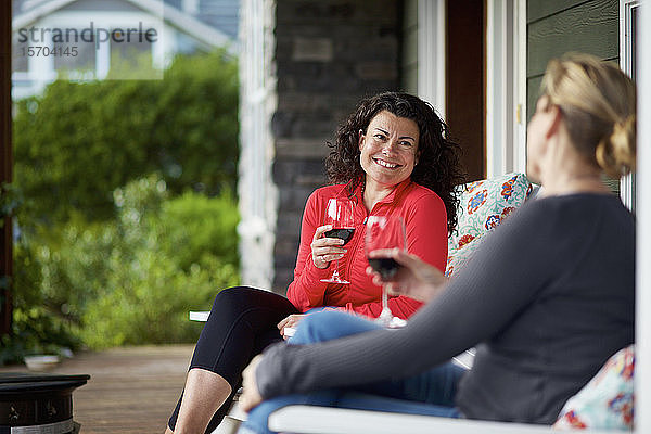 Glückliche Frauen unterhalten sich und trinken Rotwein auf der Veranda
