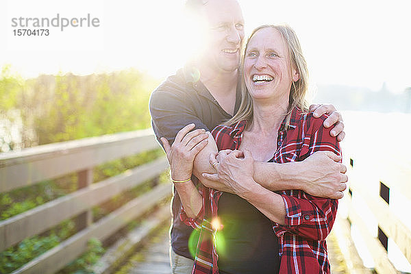 Portrait glückliches  zärtliches Paar  das sich auf einem sonnigen Sommersteg umarmt