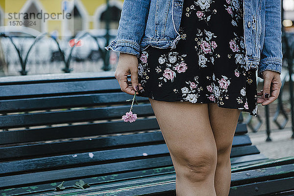Beschnittenes Bild Frau in Blumenkleid hält Blume auf Parkbank