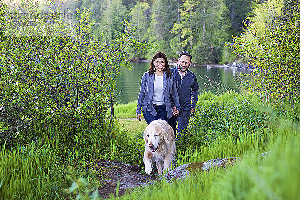 Glückliches Paar mit Hund beim Wandern am üppig grünen Seeufer  Mill Bay  British Columbia  Kanada