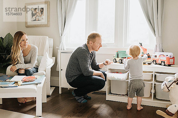 Paar beobachtet Sohn beim Spielen mit Spielzeuglastwagen im Wohnzimmer