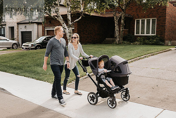 Paar nimmt Kleinkind im Kinderwagen mit zum Spaziergang in der Nachbarschaft