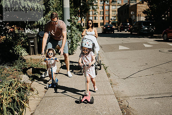 Paar und Töchter spielen in der Nachbarschaft Roller