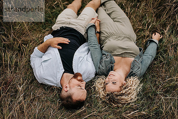 Junges Paar hält Händchen und unterhält sich auf braunem Gras