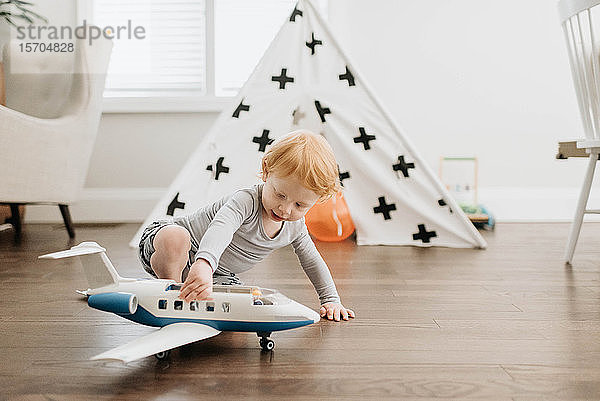 Kleinkind spielt mit Spielzeugflugzeug im Wohnzimmer