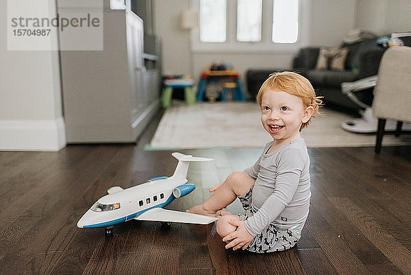 Kleinkind spielt mit Spielzeugflugzeug im Wohnzimmer