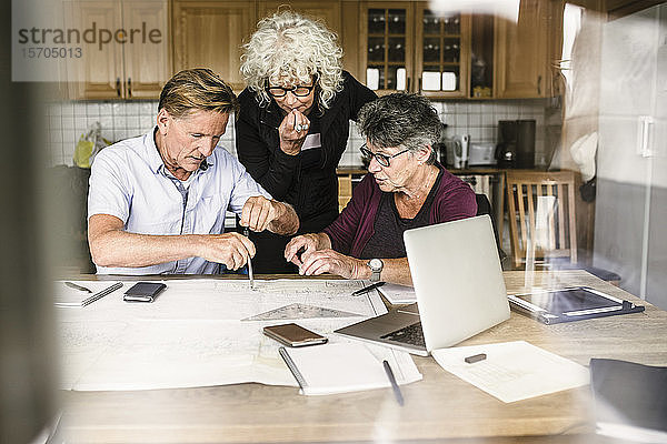 Weibliche Ausbilderin erklärt älteren Mann und Frau über Laptop am Tisch während des Navigationskurses