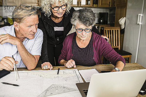 Weibliche Ausbilderin erklärt älteren Mann und Frau über Laptop am Tisch während des Navigationskurses