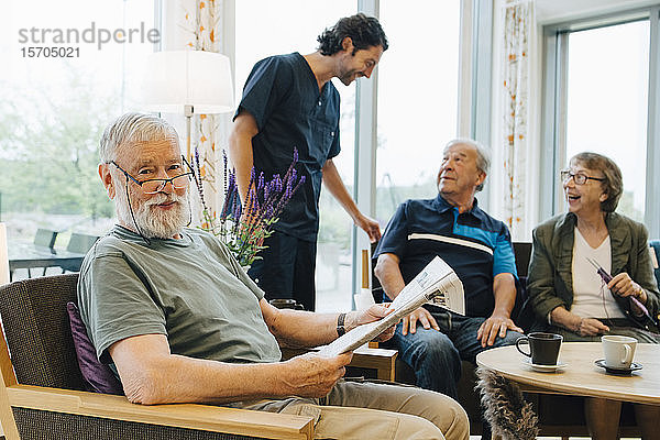 Porträt eines älteren Mannes im Ruhestand  der mit Zeitung auf einem Sessel sitzt  von Freunden und Pfleger im Altenpflegeheim