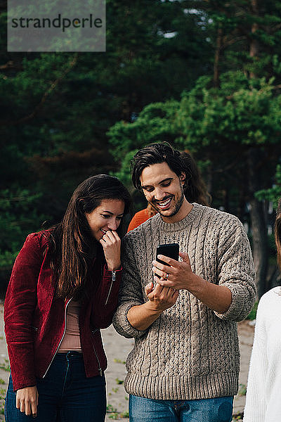 Lächelnder Mann zeigt einem Freund sein Smartphone  während er Urlaub macht
